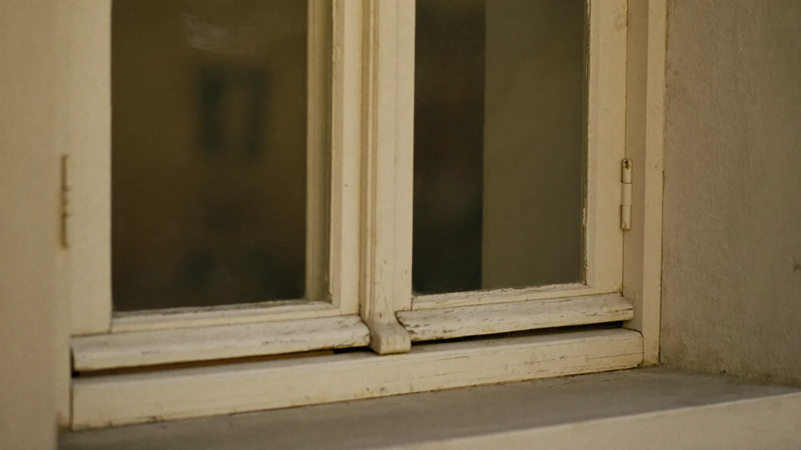 Fenêtre ancienne à cadre en bois patiné d'un appartement d'avant 1949, peinture crème vieillie, lumière douce